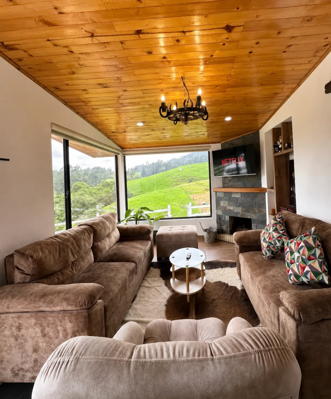 Sala de Casa Neusa con chimenea de piedra, sofas en L y ventanales al campo