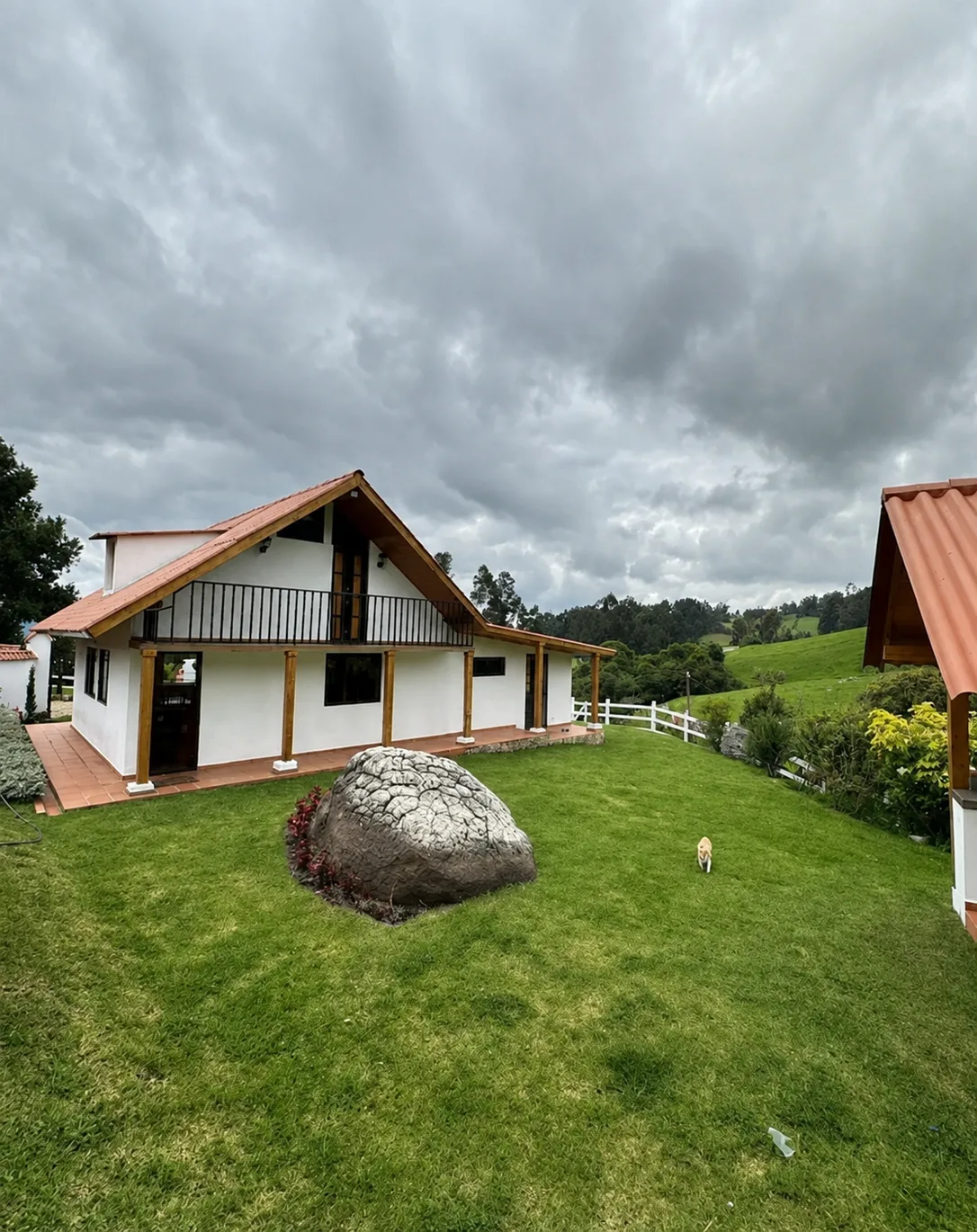 Exterior de Casa Neusa, casa de tejado a dos aguas con fachada blanca y vigas de madera, rodeada de cesped