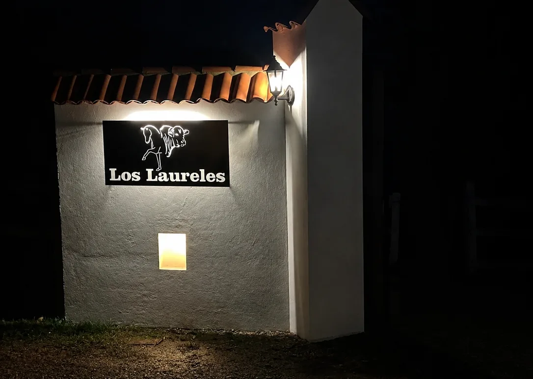 Acceso a Casa Neusa de noche, con el muro iluminado y el letrero Los Laureles