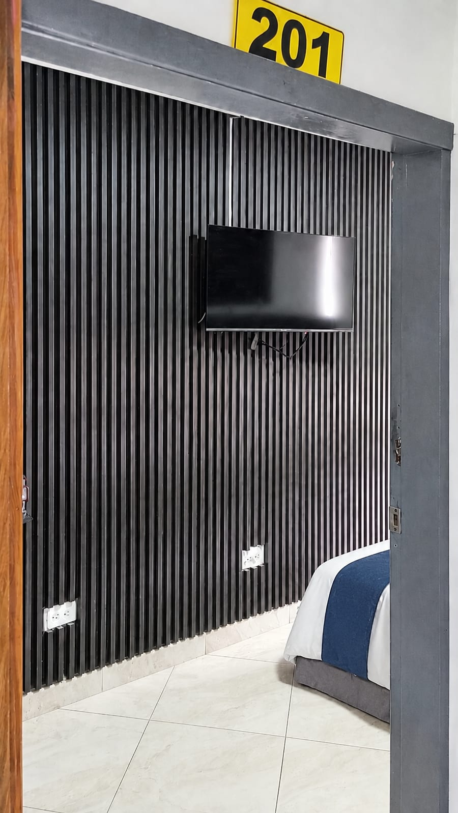 Entrada de la habitación 201 con la placa del numero y el televisor en la pared de listones