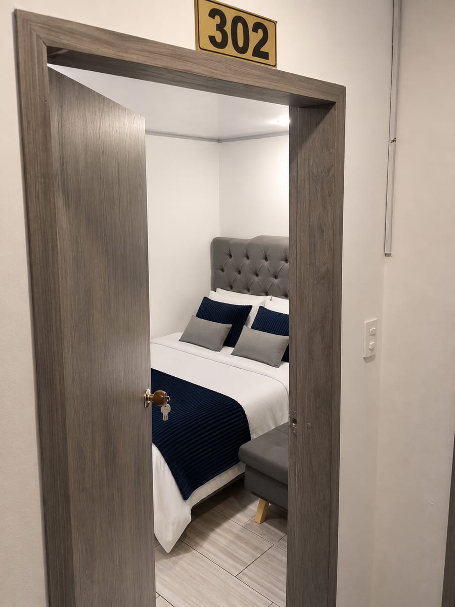 Puerta abierta de la habitación 302 con la placa del numero y la cama al fondo