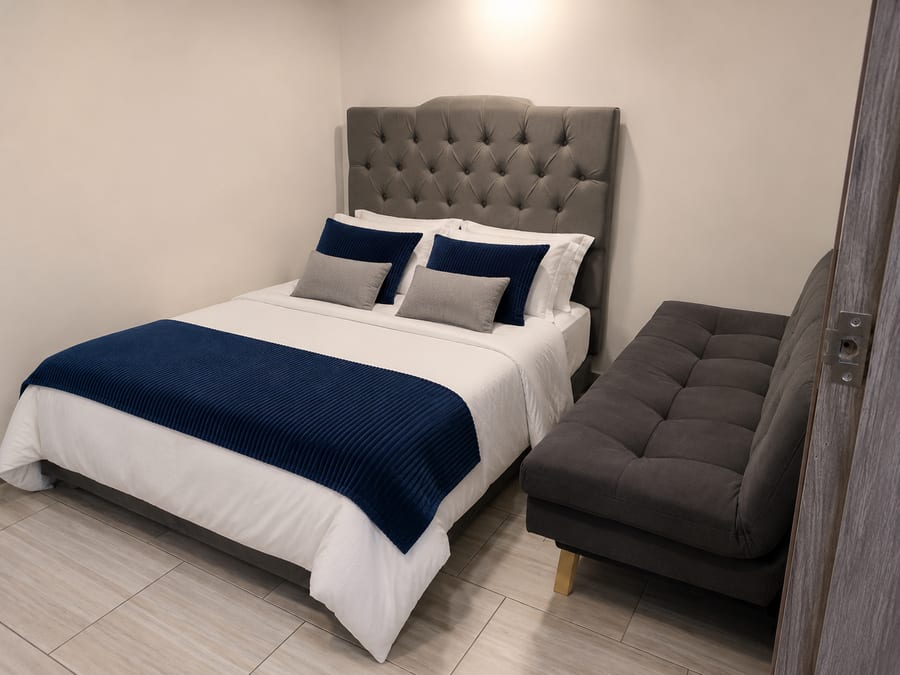 Habitación 302 con cama doble de cabecero capitone gris y sofa cama al lado